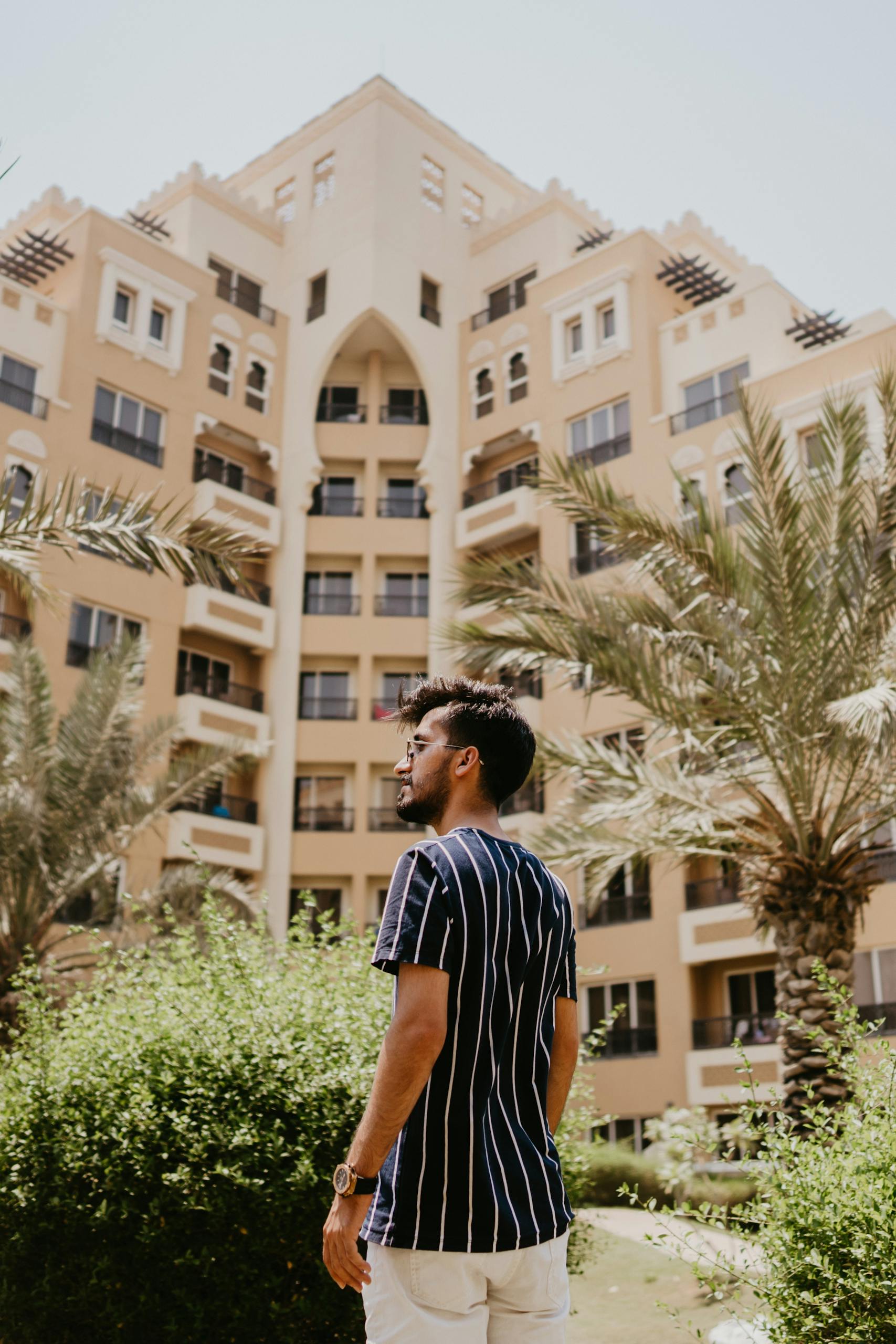 Man standing in front of luxurious Dubai hotel surrounded by palm trees, capturing urban exploration vibe.